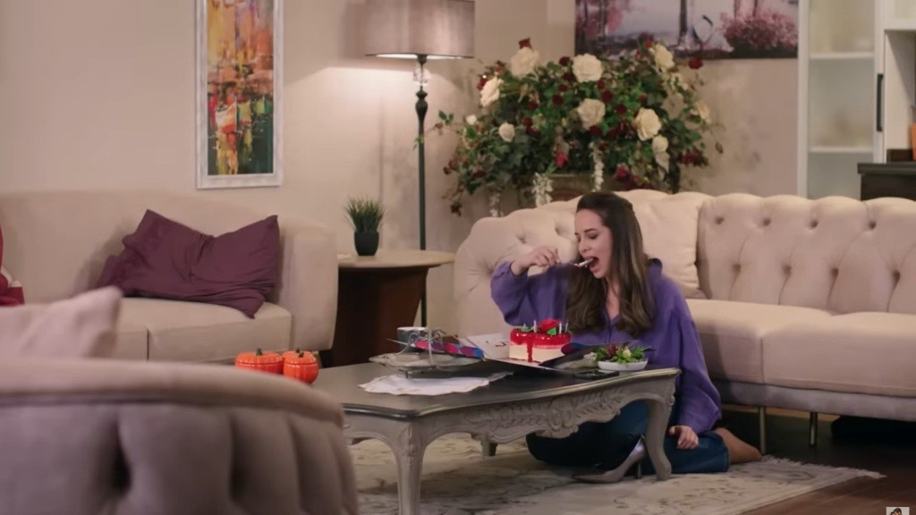 Beyza zajada się tortem, kucając w salonie przy niskim stoliku.