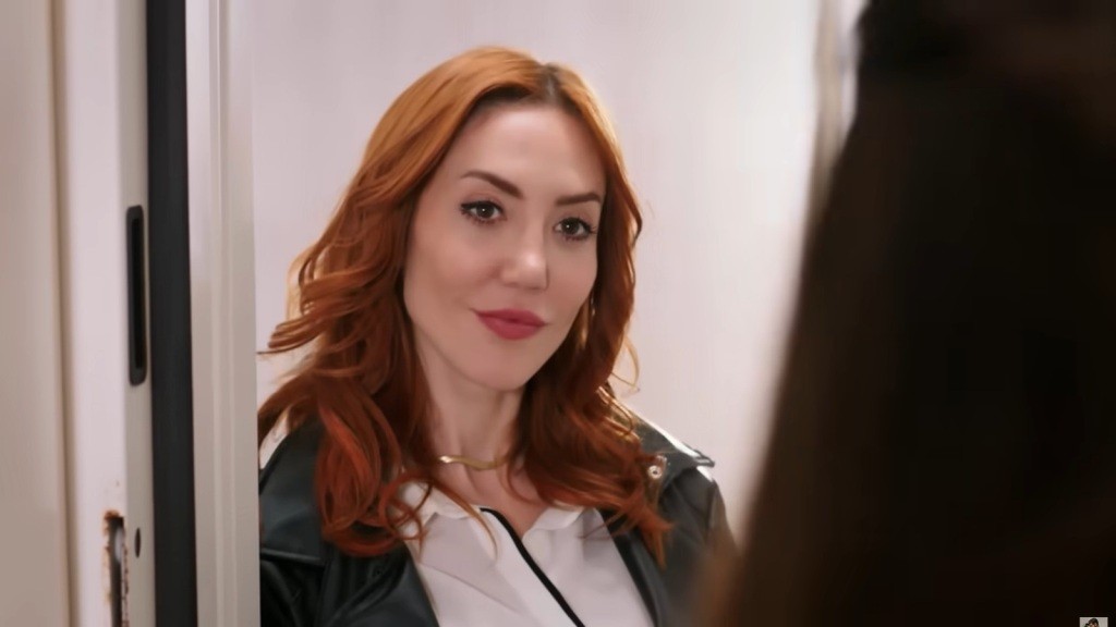 Yonca stoi przed drzwiami i uśmiecha się.