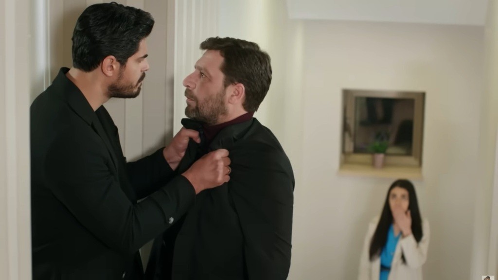 Cihan chwyta Nusreta za marynarkę. Hancer stoi na półpiętrze, skąd obserwuje scenę.