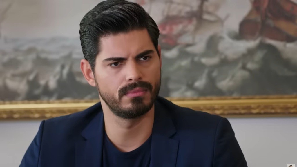 Zbliżenie na poważną twarz Cihana, który lekko marszczy brwi.