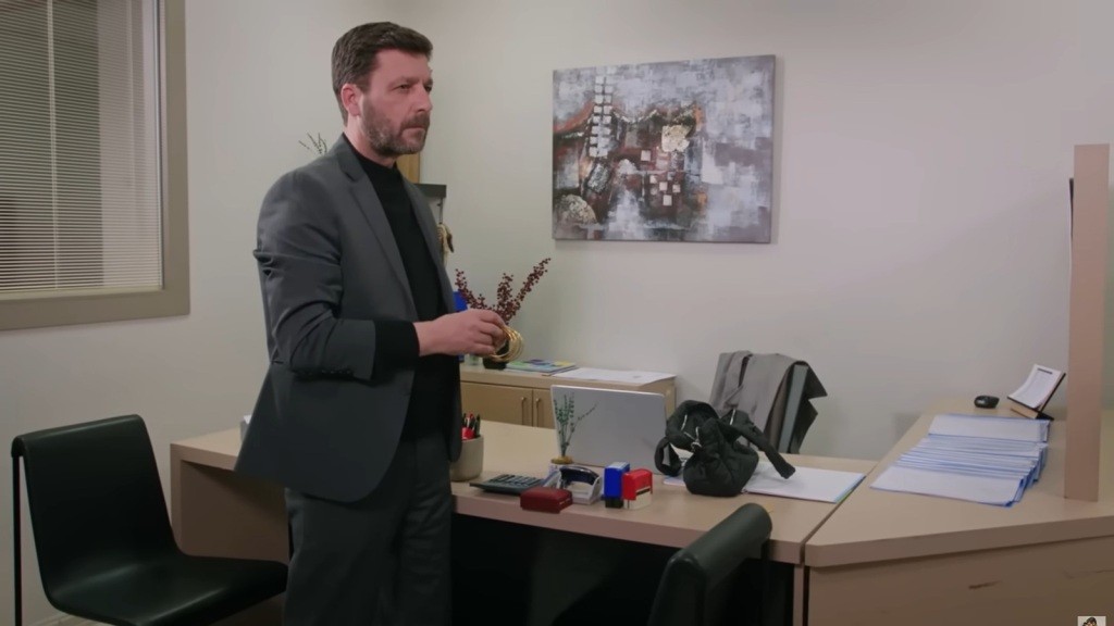 Nusret stoi obok biurka Yoncy. W rękach trzyma złote bransoletki.