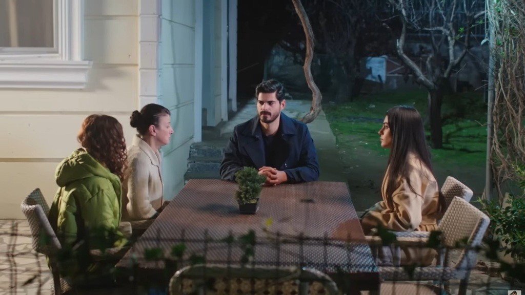 Aysu, Fadime, Cihan i Hancer siedzą przy stole na zewnątrz. Jest noc.