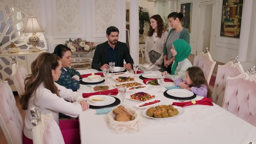 Develioglu siedzą przy stole. Fadime i Aysu stoją obok.