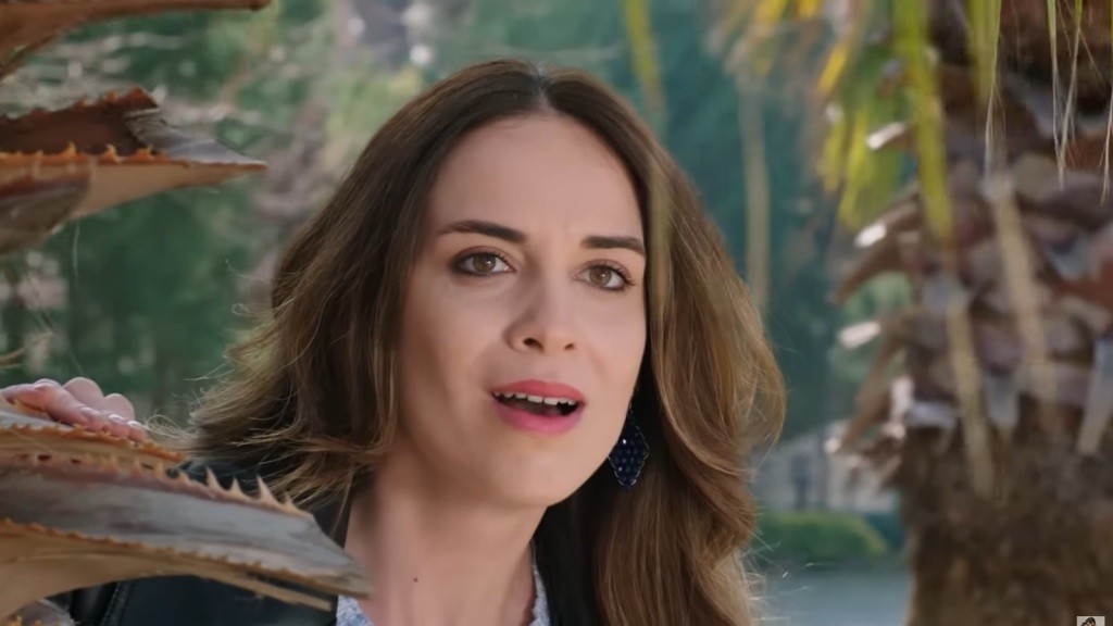 Beyza uśmiecha się z zadowoleniem, ukrywając się za pniem palmy.