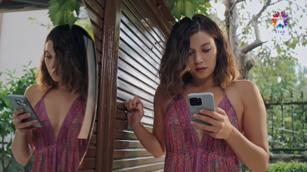 Seyran jedną ręką podpiera się o ścianę, a w drugiej trzyma telefon.