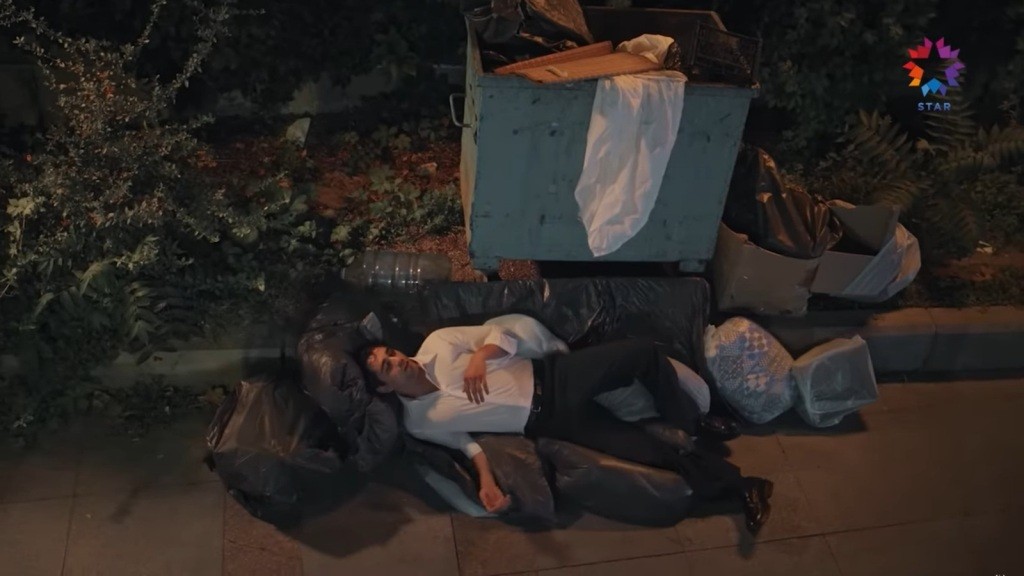 Pijany Ferit leży na workach ze śmieciami obok kontenera.