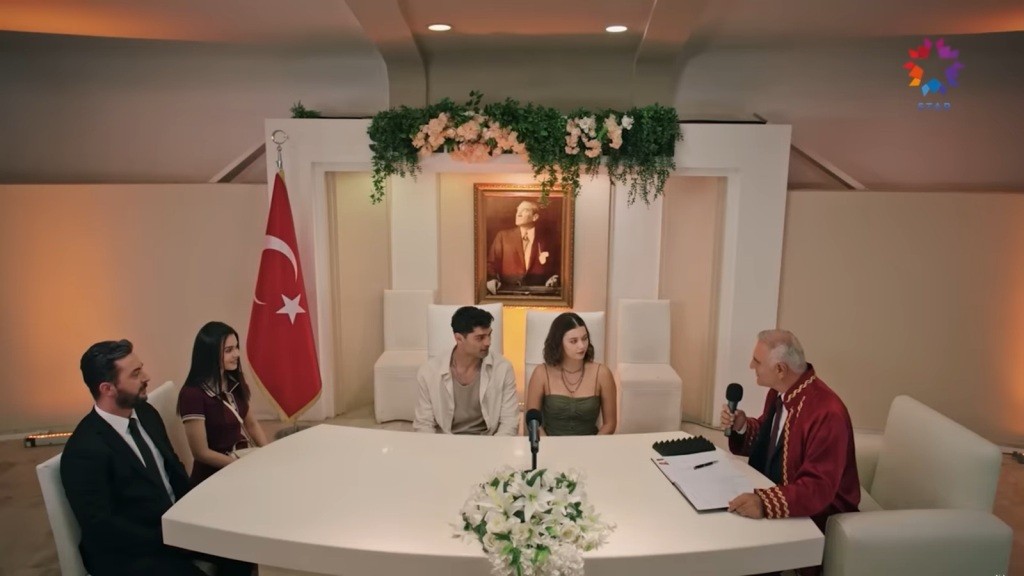 Sinan i Seyran siedzą przy stole ślubnym. Po prawej ich stronie siedzą świadkowie, a po lewej urzędnik.