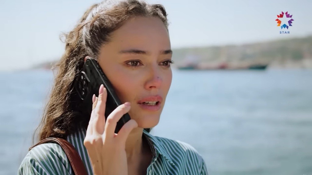 Diyar rozmawia przez telefon. W jej oczach błyszczą łzy, a za jej plecami znajduje się woda.