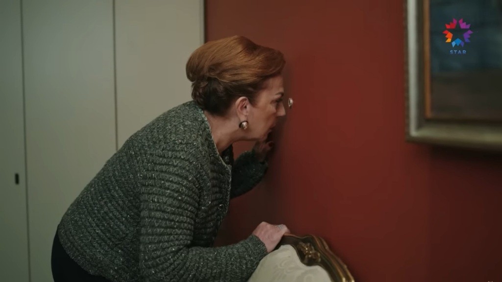 Ayla zagląda do sąsiedniego pokoju przez sekretny wizjer w ścianie.