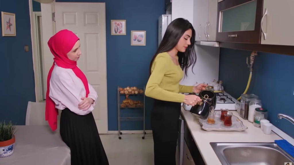 Hancer nalewa herbatę do szklanki. Za jej plecami stoi Sinem.