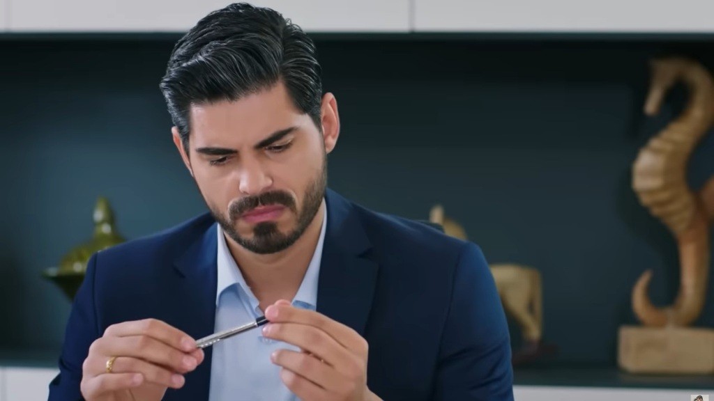 Cihan wpatruje się w trzymany w rękach długopis.