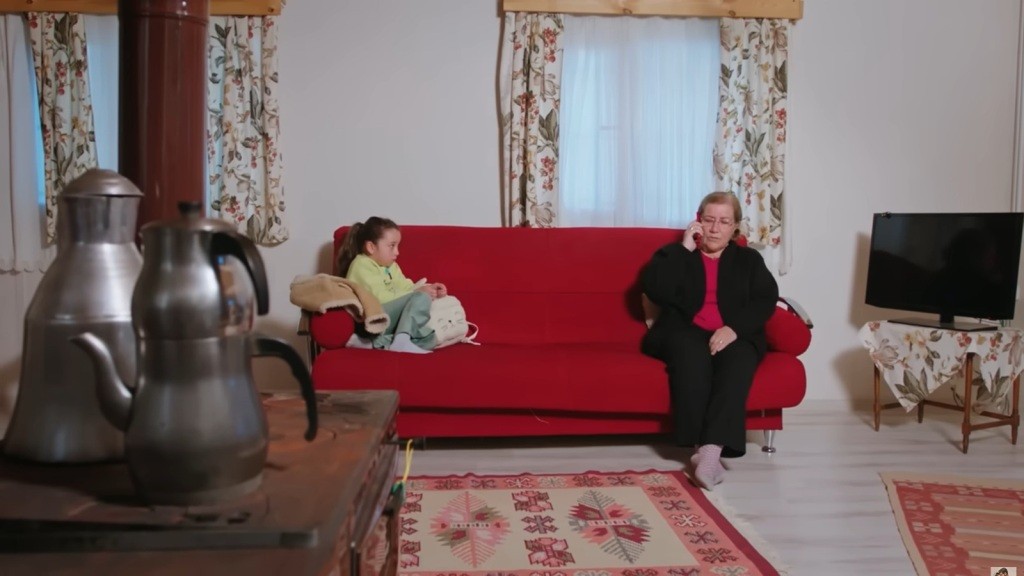 Mine siedzi na czerwonej kanapie w obcym domu, z obcą kobietą.