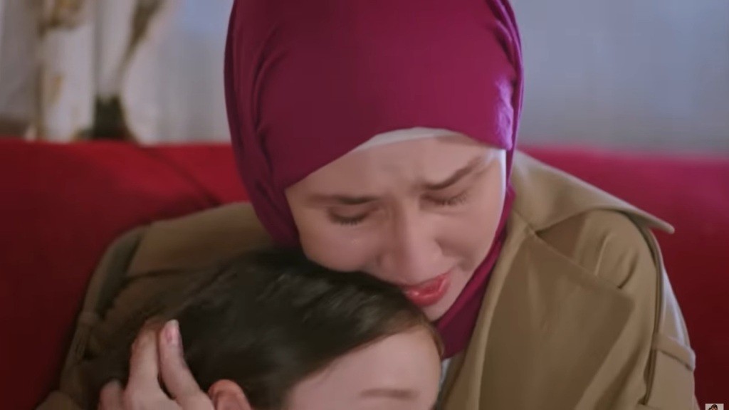 Przejmujący moment matki, noszącej kolorową chustę, obejmującej swoją córkę w emocjonalnej chwili wsparcia. Na twarzy matki widać wzruszenie, co podkreśla głęboki związek i miłość między nimi. Scena pełna ciepła i bliskości, odzwierciedlająca silne emocje rodzinne.