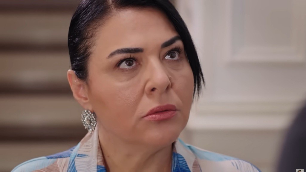 Zbliżenie na kobietę o mocnym spojrzeniu, która wyraża determinację i siłę. Jej surowa mimika i elegancki styl podkreślają charakter, wskazując na atmosferę napięcia w danej sytuacji.