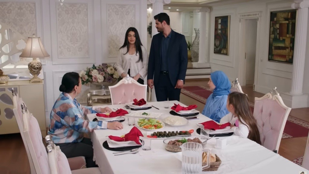 Cihan prowadzi Hancer do stołu w jadalni.