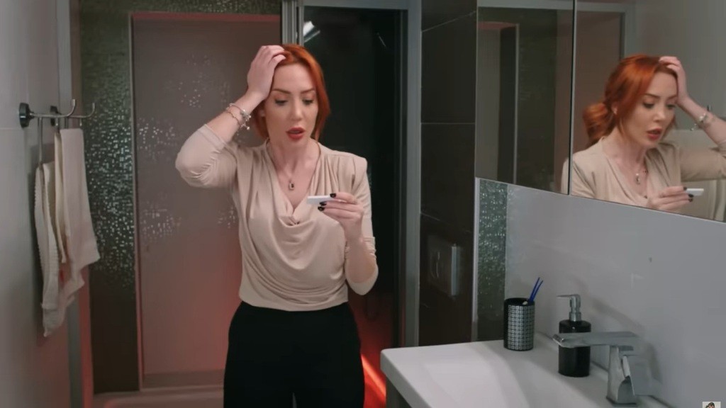 Scena w łazience. Yonca chwyta się za głowę, patrząc w wynik testu ciążowego.