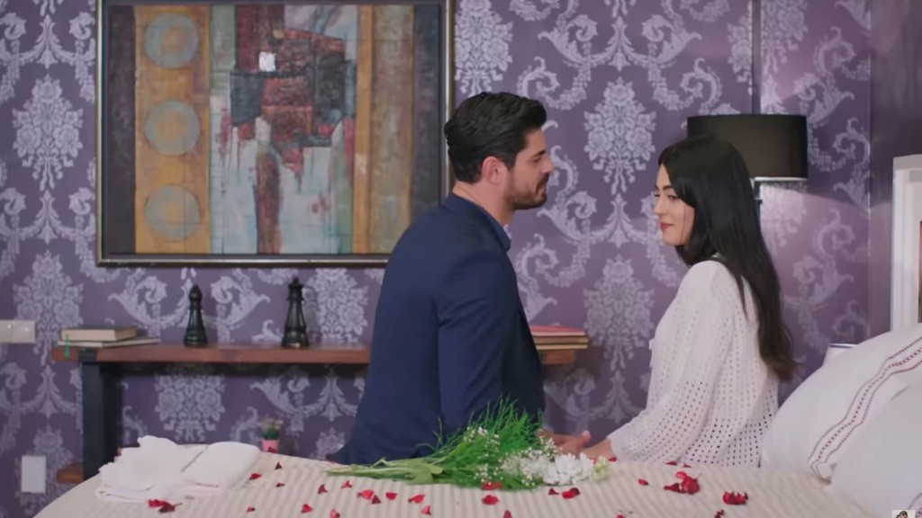 Cihan i Hancer siedzą na skraju łóżka, obsypanego płatkami czerwonych róż.