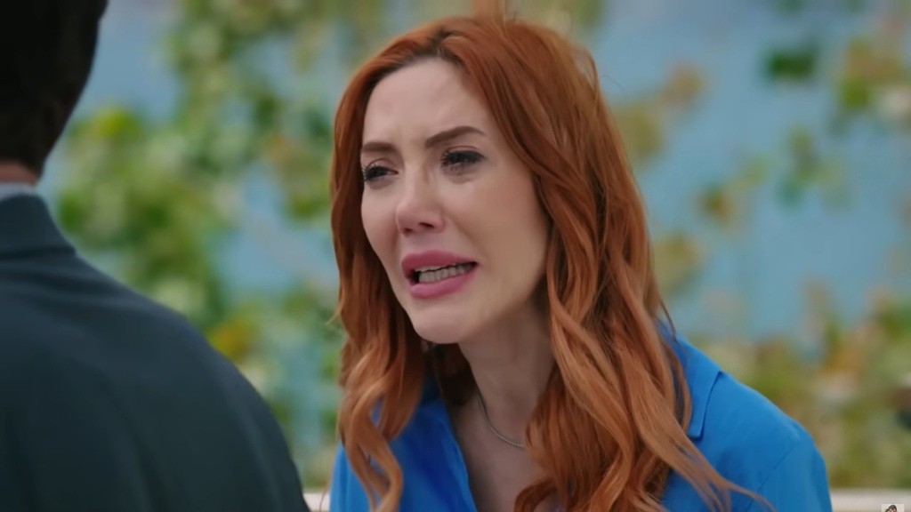 Na zdjęciu widzimy wzruszoną kobietę o rudych włosach, wyraźnie poruszoną emocjonalnie. Jej wyraz twarzy i łzy zdradzają intensywne uczucia, a sytuacja zdaje się wskazywać na chwilę kryzysu lub ważnej rozmowy.