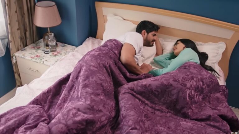 Cihan i Hancer leżą razem w łóżku pod fioletowym kocem. Intymna, spokojna chwila w przytulnej sypialni.
