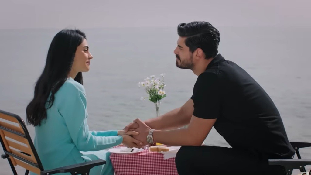 Cihan i Hancer na brzegu morza podczas romantycznego spotkania. Siedzą przy stoliku, on czule ujmuje jej dłonie i patrzy jej prosto w oczy.