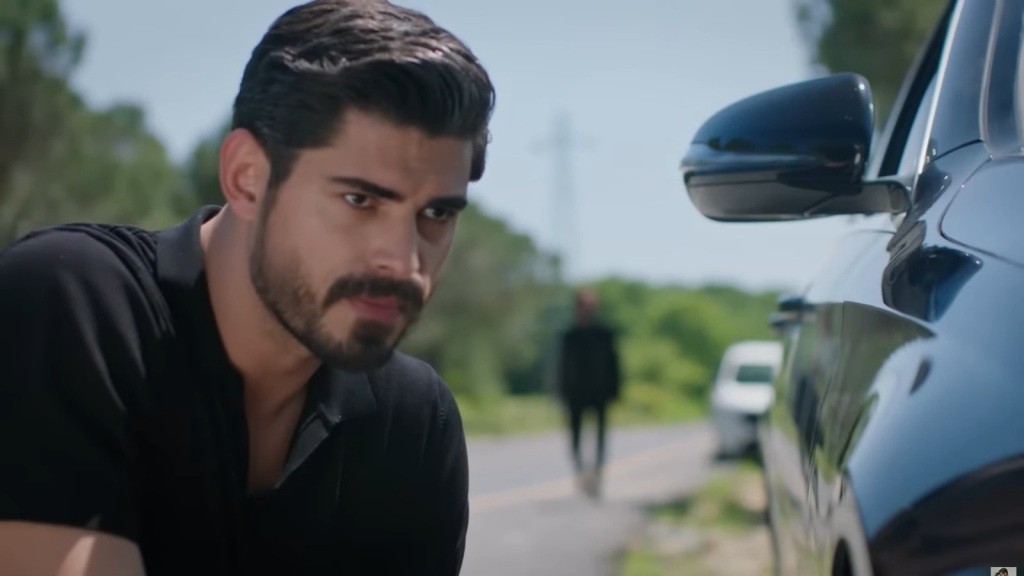 Cihan, kucając, obserwuje w lusterku bocznym zbliżającego się mężczyznę.