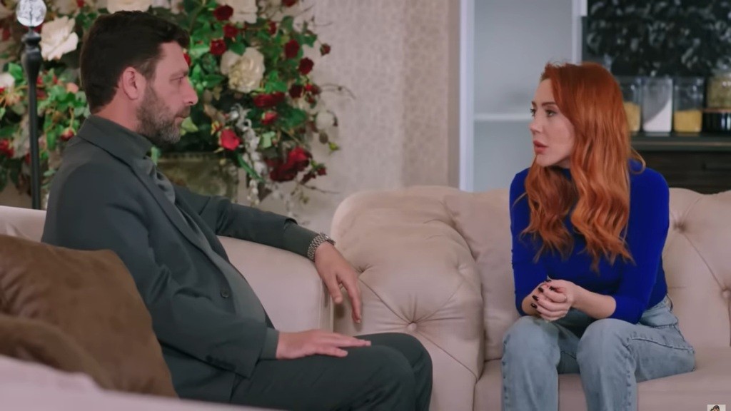 Nusret i Yonca rozmawiają. On siedzi w fotelu, a ona na kanapie.