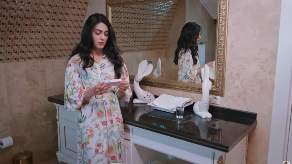 Hancer stoi przy umywalce w łazience. W rękach trzyma opakowanie tabletek antykoncepcyjnych.