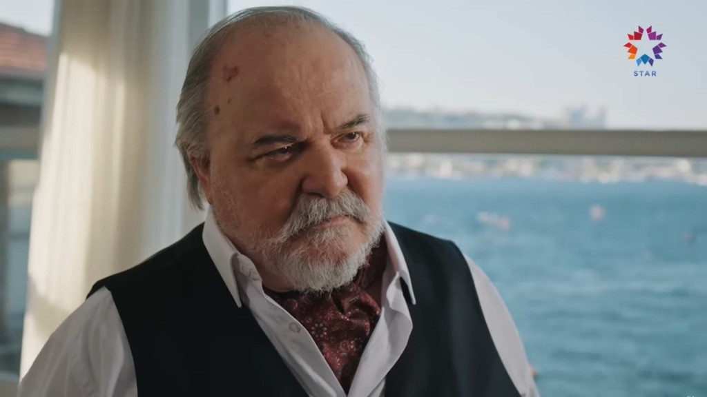 Halil spogląda poważnym wzrokiem. W tle widać niebieską taflę wody.