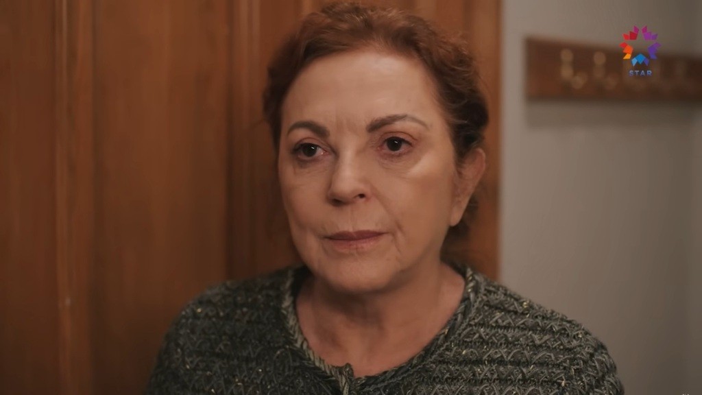 Zbliżenie na twarz Ayli, stojącej przy drzwiach.