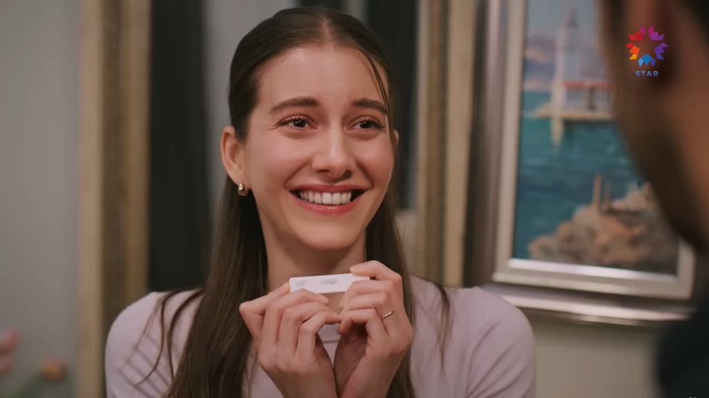 Suna trzyma test ciążowy w rękach. W okienku widać dwie kreski.