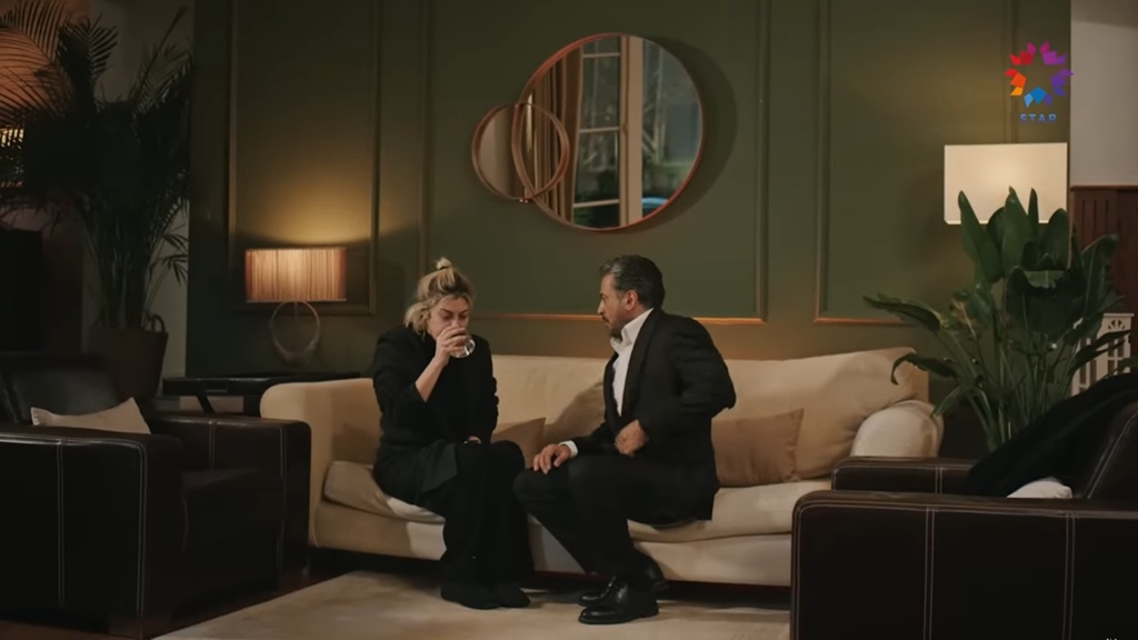 Gulgun i Orhan siedzą na kanapie. Kobieta pije wodę.