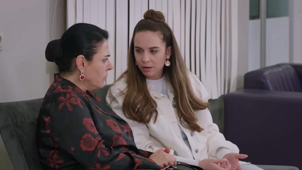 Beyza rozmawia z Mukadder, siedząc razem z nią na krzesełkach na szpitalnym korytarzu.