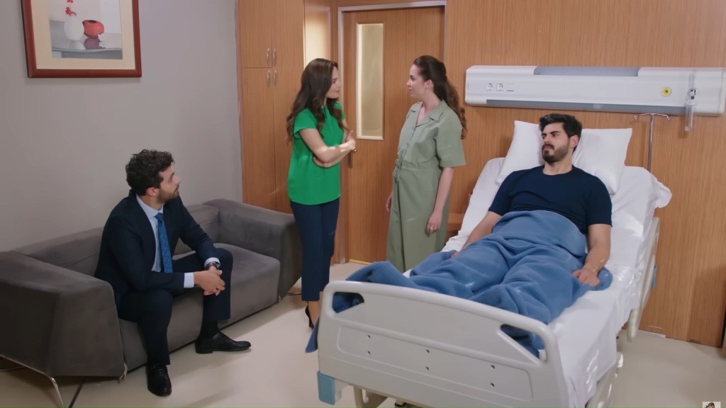 Yasemin stoi naprzeciwko Beyzy w sali Cihana. Engin siedzi na sofie.