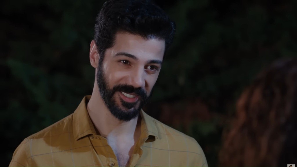Melih uśmiecha się. Za jego plecami maluje się noc.