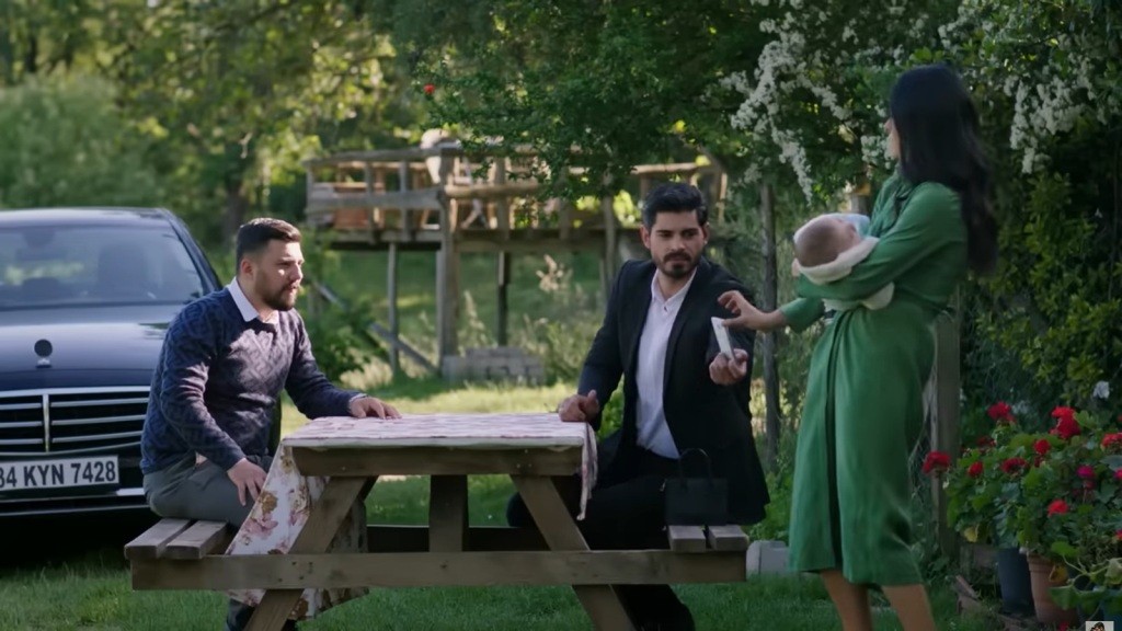 Hancer trzyma niemowlę na rękach. Siedzący na ławce Cihan podaje jej telefon. Naprzeciwko Cihana siedzi Selim, jego kolega z wojska.