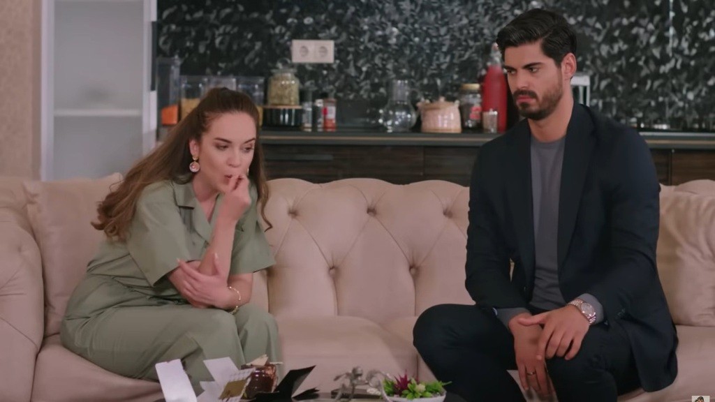 Beyza i Cihan siedzą na kanapie. Ona zajada się ciastem, a on przygląda się jej.