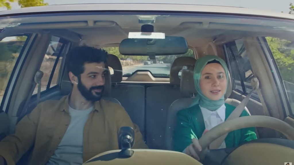 Sinem prowadzi samochód. Na fotelu obok siedzi Melih i przygląda jej się z uśmiechem.