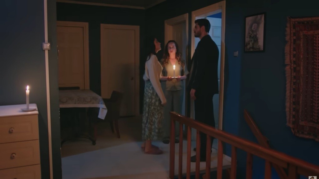 Hancer, Cihan i Beyza stoją na korytarzu przy świetle świecy — napięta, tajemnicza scena domowego wieczoru.