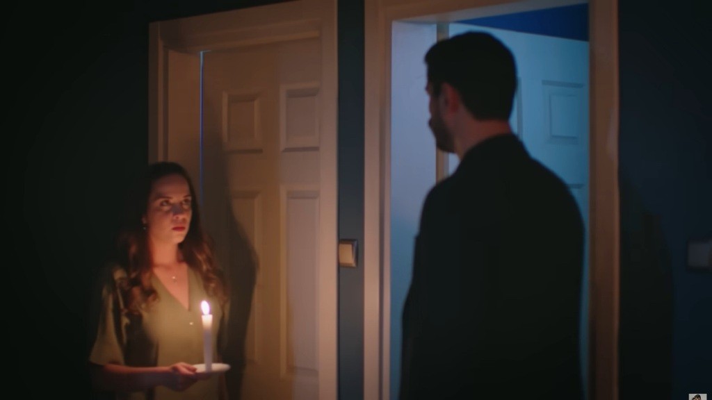 Beyza ze świecą w ręku stoi w progu naprzeciw Cihana — napięta, tajemnicza scena w półmroku.
