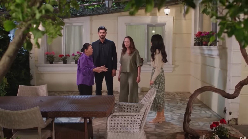 Mukadder, Cihan, Beyza i Hancer na kameralnym, oświetlonym patio z kwiatami i meblami ogrodowymi.