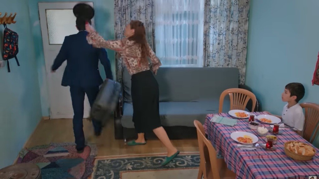 Derya zachodzi Cemila od tyłu i uderza go patelnią w głowę. Emir siedzi przy stole.