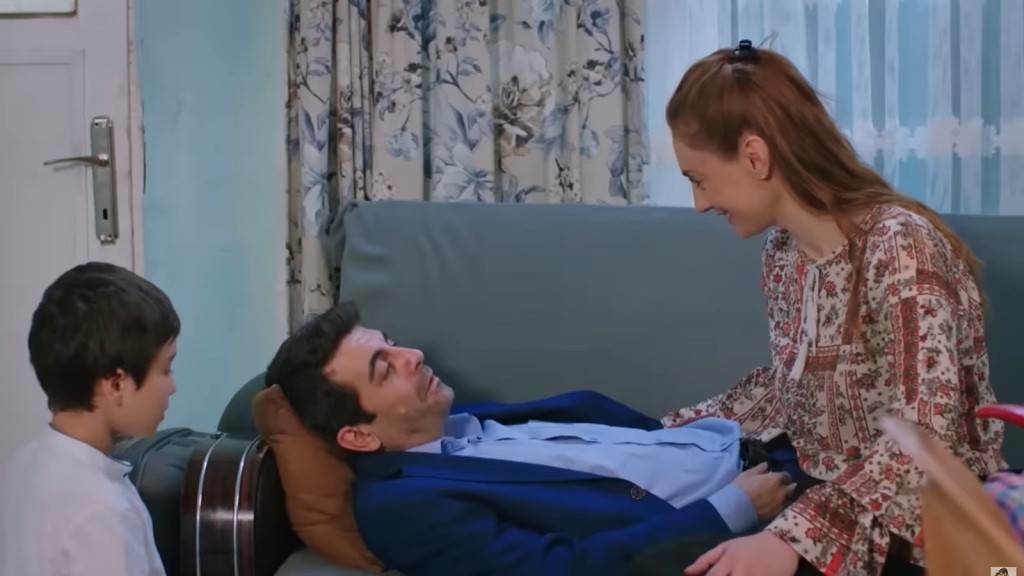 Cemil leży na kanapie. Derya i Emir są obok niego.
