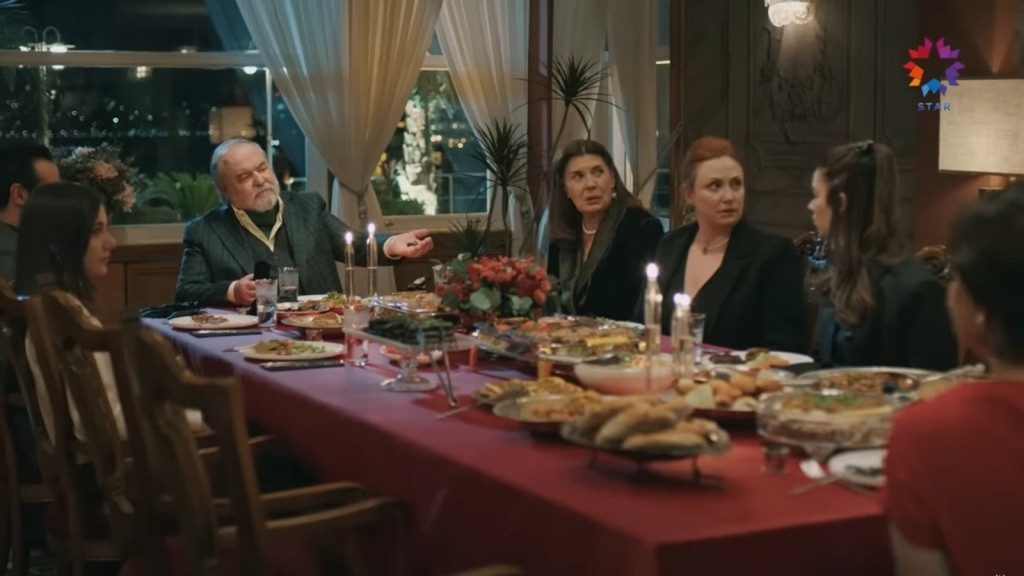 Kolacja w rezydencji. Halis siedzi na czele stoły. W otwartej dłoni trzyma kamienie jubilerskie.