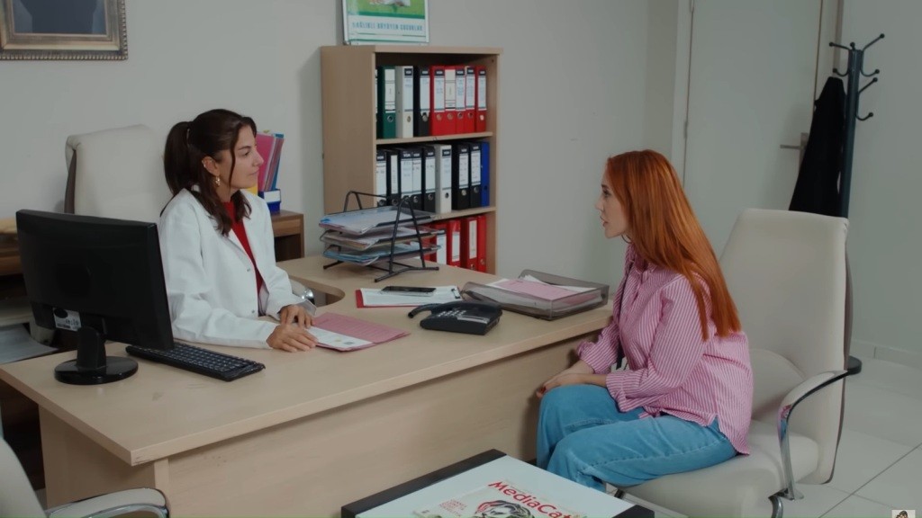 Yonca siedzi przy biurku lekarki.