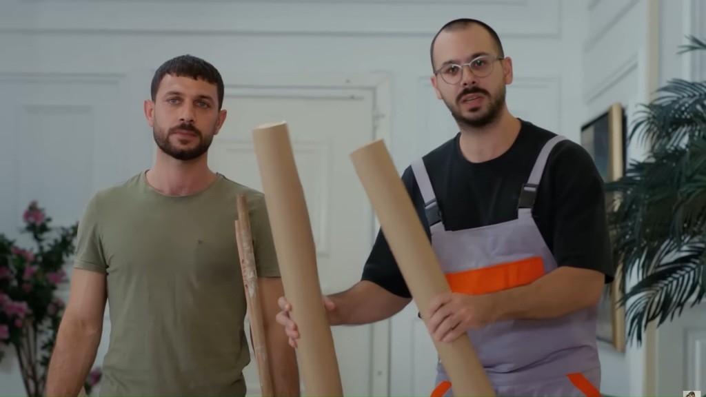 Pracownicy stoją w holu. Jeden z nich trzyma w rękach zwinięte w rulon pasy tapety.