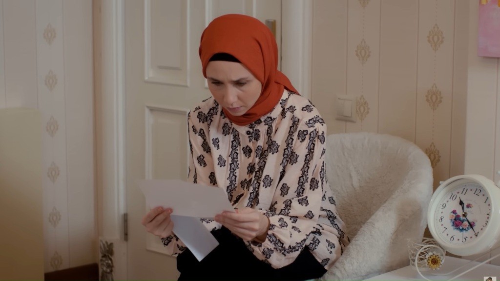 Sinem siedzi w niewielkim beżowym fotelu i czyta list.