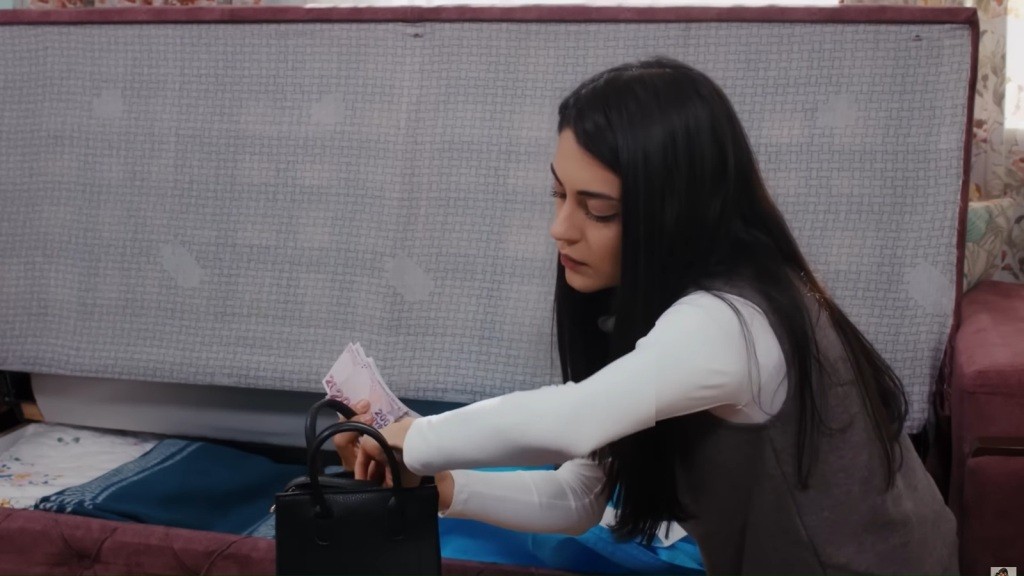 Hancer kuca przy schowku w kanapie. W ręku trzyma pieniądze.