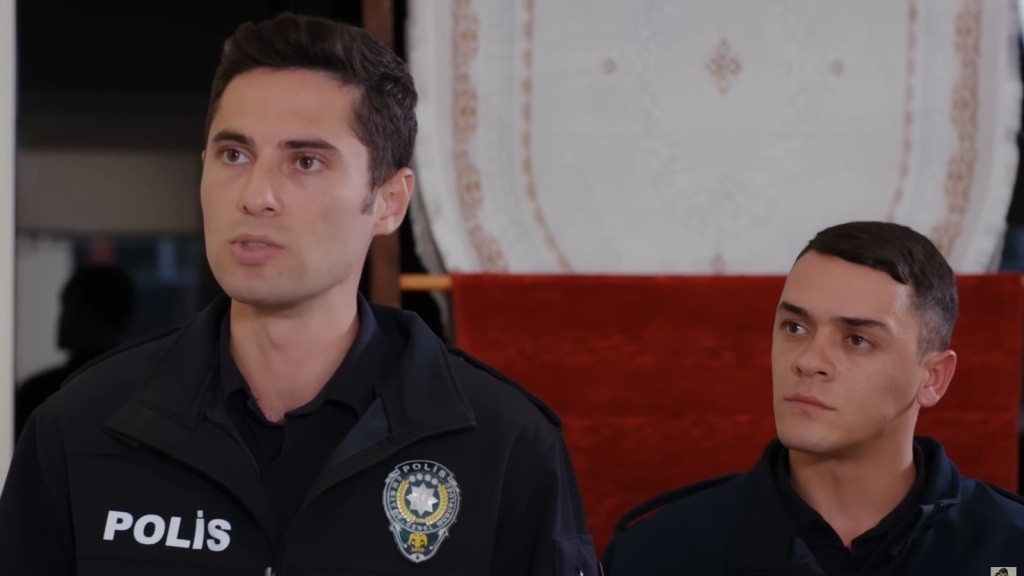Portret dwóch młodych policjantów w mundurach na tle wnętrza z dekoracyjnym dywanem.