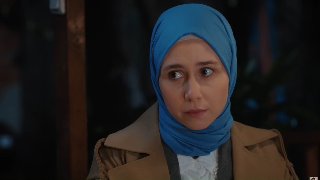 Sinem ma na głowie niebieski hidżab. Na jej twarzy maluje się poważny i refleksyjny wyraz.