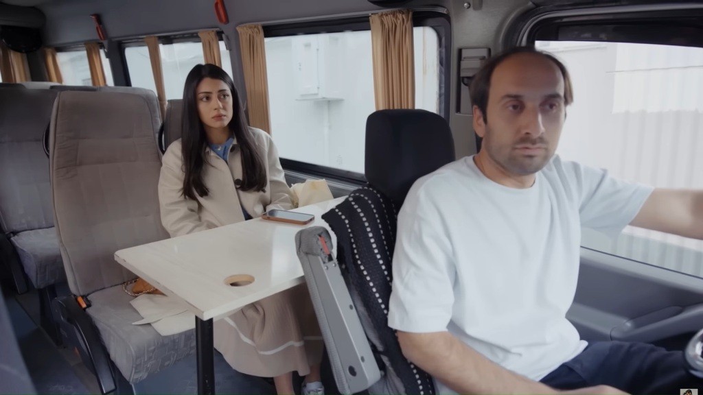 Hancer siedzi jako pasażerka w autobusie. Na pierwszy planie widać kierowcę w białym t-shircie.